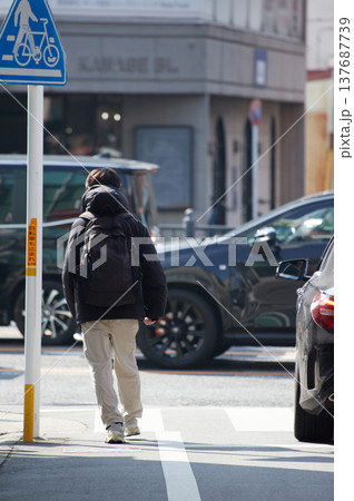 冬の朝の都市の繁華街で歩く通勤中の若い男性と通勤時間の車の列の様子 冬の朝の都市の繁華街で歩く通勤中の若い男性と通勤時間の車の列の様子 137687739