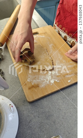 Individual shapes gingerbread dough with a cookie cutter on a wooden board, surrounded by flour and kitchen utensils in a home kitchen setting 137688043