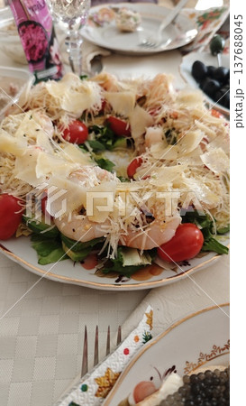 Colorful salad with cherry tomatoes, cheese, and greens arranged on a decorative plate, surrounded by additional dishes on a dining table Colorful salad with cherry tomatoes, cheese, and greens arranged on a decorative plate, surrounded by additional dishes on a dining table 137688045
