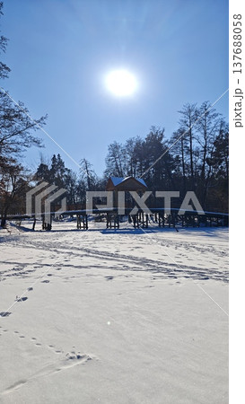 Snow-covered landscape with a wooden cabin on stilts surrounded by trees under a bright sun in a clear blue sky during winter season 137688058