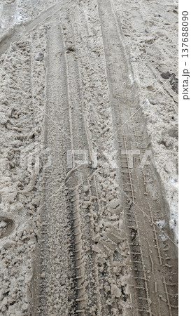 Tire tracks and footprints are visible on a snow-covered dirt road, indicating recent vehicle and pedestrian movement in a winter setting Tire tracks and footprints are visible on a snow-covered dirt road, indicating recent vehicle and pedestrian movement in a winter setting 137688090