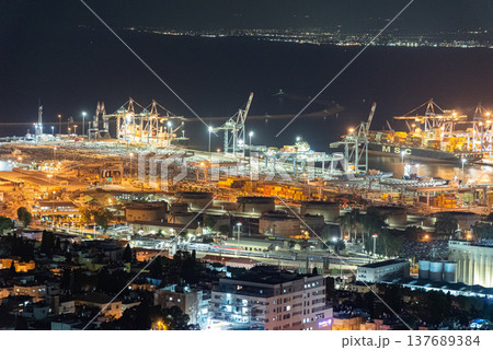 Night view of large cargo port with container ships, cranes and stacked containers illuminated by industrial lights. Maritime transport, logistics and global trade concept. Night view of large cargo port with container ships, cranes and stacked containers illuminated by industrial lights. Maritime transport, logistics and global trade concept. 137689384