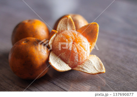 Fresh peeled mandarin with whole fruits on wooden table in soft natural light, close-up still life. 137690877