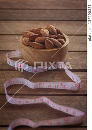 Almonds in a wooden cup on a wood plate with a measuring tape, symbolizing healthy diet control. 137690881