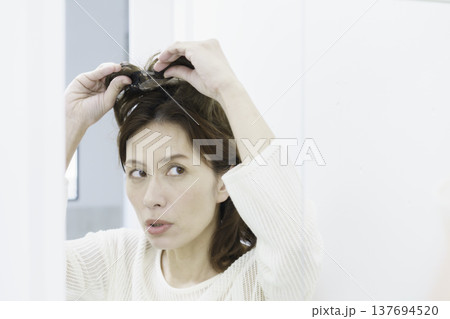 鏡を見ながら、部分ウィッグをつけようとするミドルエイジの日本人女性 137694520