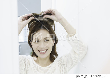 鏡を見ながら、部分ウィッグをつけようとする笑顔のミドルエイジの日本人女性 137694526