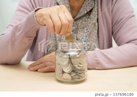 Retired elderly woman putting coins money in piggy bank and worry about monthly expenses and treatment fee payment. Retired elderly woman putting coins money in piggy bank and worry about monthly expenses and treatment fee payment. 137696180