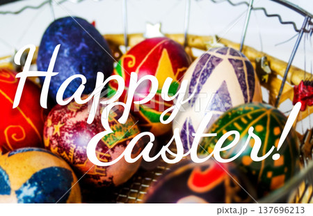 Happy Easter greeting card concept. Close-up of traditional painted Easter eggs pysanky in a wicker basket with elegant white Happy Easter text overlay Happy Easter greeting card concept. Close-up of traditional painted Easter eggs pysanky in a wicker basket with elegant white Happy Easter text overlay 137696213