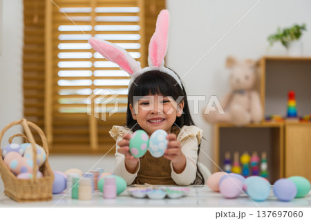 happy preschool child girl wearing bunny ears holding colorful egg while celebrating on easter day on table at home 137697060