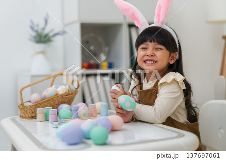 happy preschool child girl wearing bunny ears holding colorful egg while celebrating on easter day on table at home happy preschool child girl wearing bunny ears holding colorful egg while celebrating on easter day on table at home 137697061