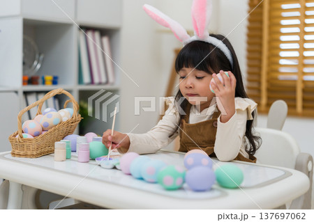 preschool child girl wearing bunny ears painting and decorating colorful egg at home on easter day preschool child girl wearing bunny ears painting and decorating colorful egg at home on easter day 137697062