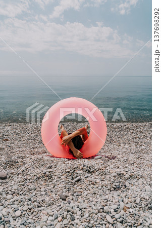 Summer relaxation beach holiday concept, person lying down resting inside pink inflatable ring on beautiful pebble coastline. Summer relaxation beach holiday concept, person lying down resting inside pink inflatable ring on beautiful pebble coastline. 137698292