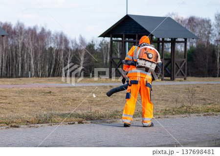 Municipal worker cleaning asphalt road with power leaf blower 137698481