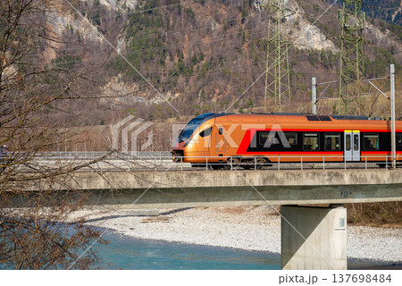 Modern orange passenger train crossing concrete bridge Modern orange passenger train crossing concrete bridge 137698484