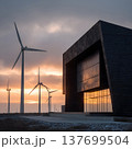 Minimalist black modern building with solar facade, standing near wind farm with multiple turbines, dramatic sunset light 137699504