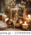 Close-up of a glass of champagne with rising bubbles, blurred festive candles and gold decor behind, soft elegant bokeh  137699509
