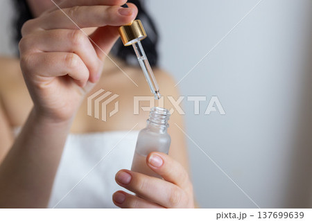 Woman using glass dropper to apply facial serum from cosmetic bottle, skincare routine and beauty treatment concept 137699639