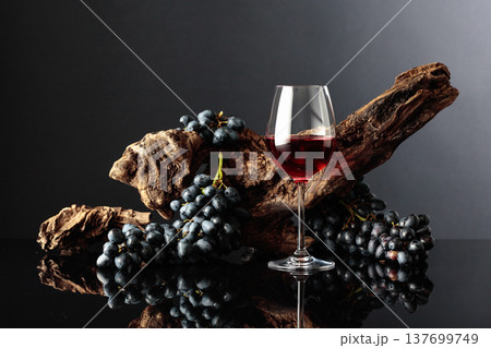 Glass of red wine with an old snag and blue grapes. Glass of red wine with an old snag and blue grapes. 137699749