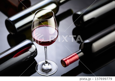 Glass and bottles of red wine on a black reflective background. Glass and bottles of red wine on a black reflective background. 137699779