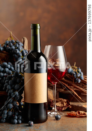 Bottle of red wine with blue grapes on a brown background. 137699798