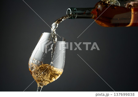 Pouring white wine from a bottle into a glass. 137699838