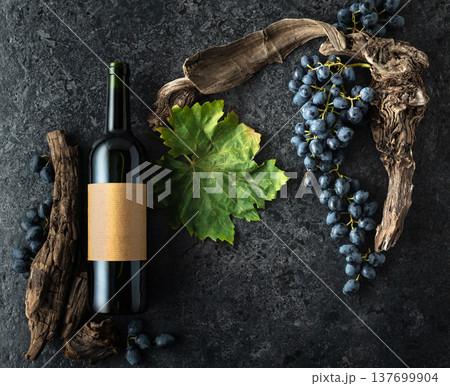 Bottle of red wine, blue grapes, and old vine snags on a black stone background. Bottle of red wine, blue grapes, and old vine snags on a black stone background. 137699904