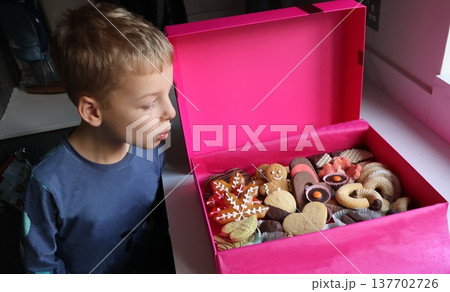 A boy is looking into a pink box full of cookies 137702726