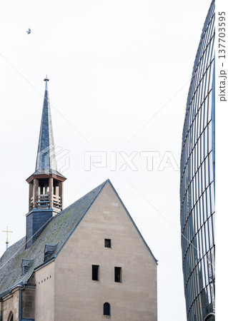 Antoniterkirche stands beside a modern urban building in Cologne, Germany. The church features a tall spire and traditional architecture, contrasting with the glass structure. Antoniterkirche stands beside a modern urban building in Cologne, Germany. The church features a tall spire and traditional architecture, contrasting with the glass structure. 137703595