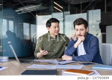 Mature asian business man offering support and empathy to a distressed male colleague in a modern office, showing teamwork and mental wellness at the workplace 137703694