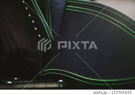 A detailed horizontal shot of a premium black leather vehicle seat featuring vibrant neon green double stitching and metallic stud accents. 137705835