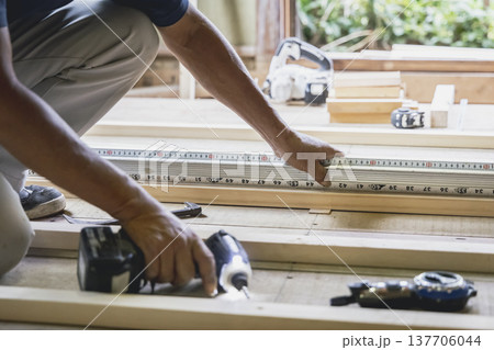 木造住宅の建築現場でメジャーを使い木材の寸法を測る大工の手元	 137706044