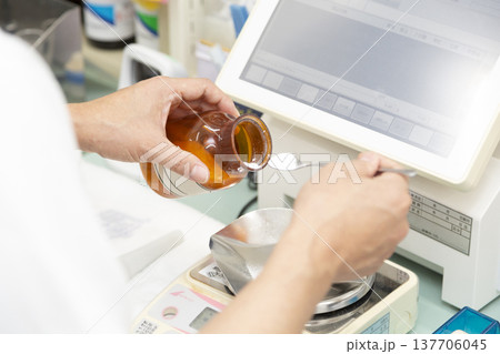 薬局や病院で電子天秤を用いて薬品を正確に計量する調剤風景 137706045