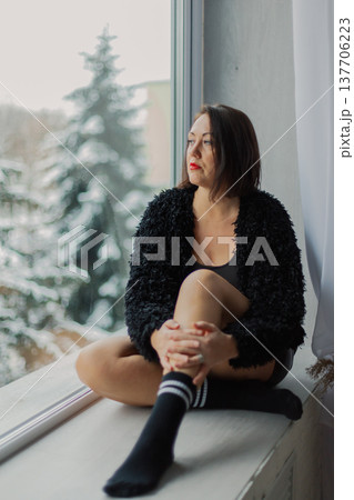 Beautiful woman posing on a large window in a Beautiful woman posing on a large window in a 137706223