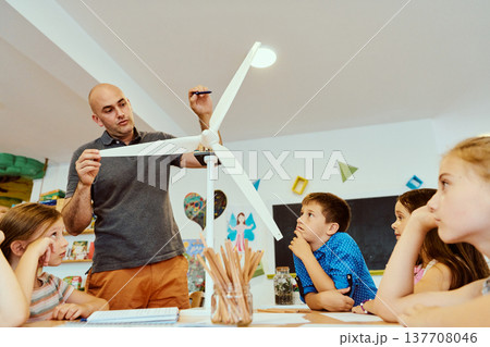 Teacher demonstrates a model wind turbine to curious children during a STEM lesson in a classroom 137708046