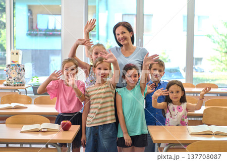 Teacher and elementary students smiling and waving together in a bright classroom group photo Teacher and elementary students smiling and waving together in a bright classroom group photo 137708087