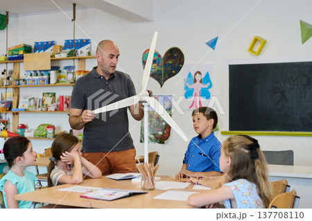 Teacher demonstrating a wind turbine model to elementary students during a hands-on STEM classroom lesson 137708110