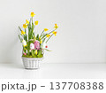 Easter composition with flowers in basket and painted eggs on white table. Spring flowers daffodils and hyacinths in a white basket. Copy space. 137708388