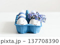 Easter composition with eggs in a blue cardboard box on white background. Couple of funny eggs with painted faces and flowers. 137708390