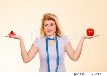 Woman with measuring tape choosing what to eat 137709908