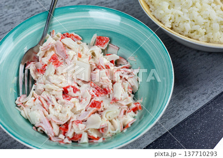 Bowl of creamy crab stick mixture with mayonnaise and cream cheese in white ceramic bowl. Preparation stage for homemade sushi rolls and onigiri filling. Fresh ingredients on kitchen table 137710293