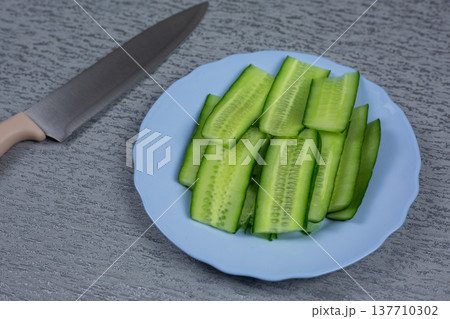 Fresh cucumber sliced lengthwise on blue plate with knife blade visible in background. Vegetable transformed into healthy noodle alternative. Preparation for low carb meal or salad 137710302