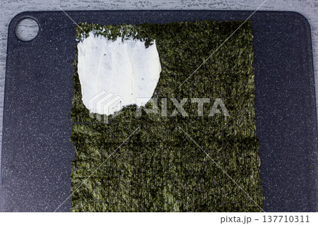 Nori sheet with cream cheese spread on one quarter section. First step in making lazy sushi sandwich. Simple recipe tutorial showing ingredient placement for homemade Japanese snack 137710311