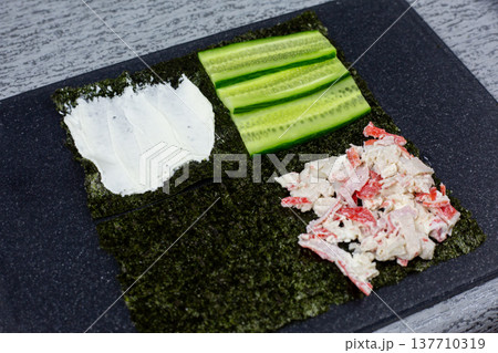 Nori sheet transformed into base for global fusion flavors. Cream cheese, cucumber, and crab mixture arranged in quarters. Creative culinary experiment blending Asian and Western ingredients 137710319