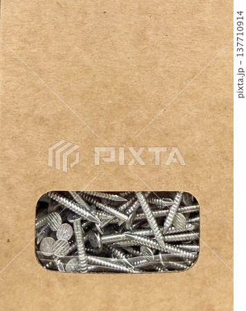 Cardboard box with metal nails visible through transparent window, minimal packaging close-up. Cardboard box with metal nails visible through transparent window, minimal packaging close-up. 137710914