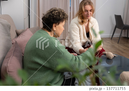 Mother and daughter knitting together at home on sofa Mother and daughter knitting together at home on sofa 137711755