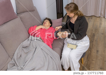 Caregiver measuring blood pressure of senior woman at home 137711760