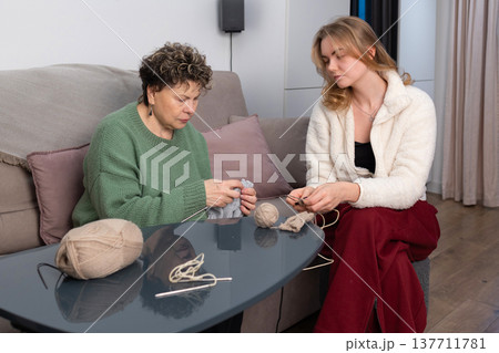 Mother and daughter knitting together at home on sofa 137711781
