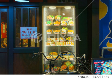 Osaka, Japan - Sep 21 2024, A close-up view of the glass showcase of a restaurant with wax models of Japanese cuisine, with a bicycle parked in foreground, without people, at evening, Osaka, Japan Osaka, Japan - Sep 21 2024, A close-up view of the glass showcase of a restaurant with wax models of Japanese cuisine, with a bicycle parked in foreground, without people, at evening, Osaka, Japan 137711825