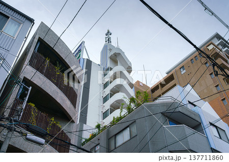 Osaka, Japan - Sep 21 2024, Panoramic view from the bottom up to the facade of various multi-storey apartment buildings, with grey cloudy sky and wires, at daytime, without people, Osaka, Japan 137711860