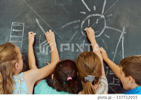 Four children drawing a sun and shapes on a classroom chalkboard during a creative school activity Four children drawing a sun and shapes on a classroom chalkboard during a creative school activity 137712055